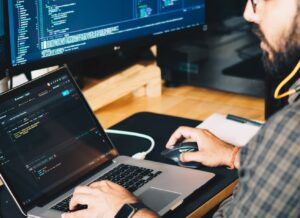 Programista przy laptopie, na monitorze otwarty kod źródłowy